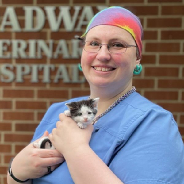 Liz posing for a picture outdoors with a kitten in front of a brick wall